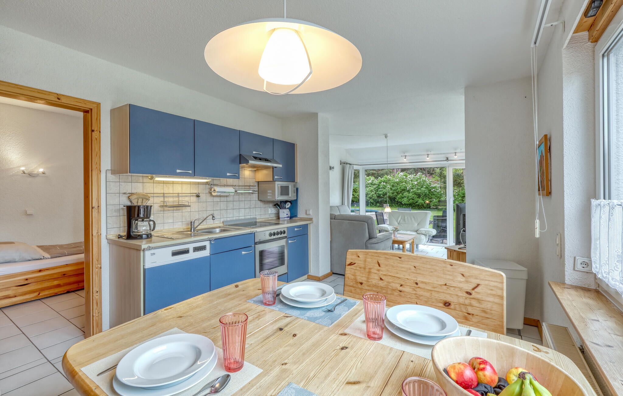 A compact kitchen with blue cabinets, a dining table set with plates and glasses, and a fruit bowl.