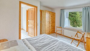 A bedroom with a bed, wooden wardrobe, a chair, a radiator, and a window with curtains. - Ferienwohnung Pruchten (Pruchten)
