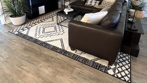Una sala de estar moderna con un sofá marrón oscuro, un televisor de pantalla plana, un ventilador de techo y cortinas estampadas.
