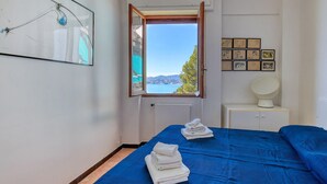 A bedroom with a bed, a window with a view, a radiator, and a wall with framed pictures.