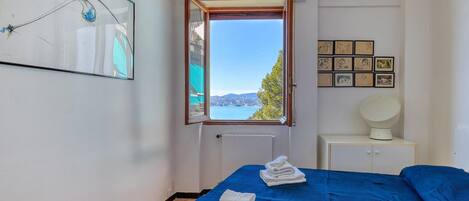 Un dormitorio con cama, ventana con vistas, radiador y un muro con cuadros.
