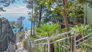 A staircase leading to a balcony overlooking a body of water, surrounded by trees and greenery.