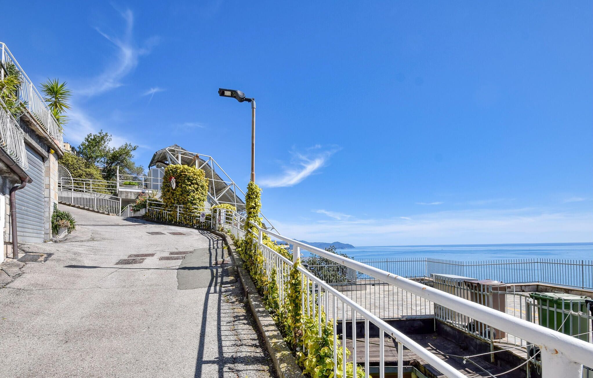 Une rue côtière avec une rambarde en métal, un lampadaire et une vue sur la mer.