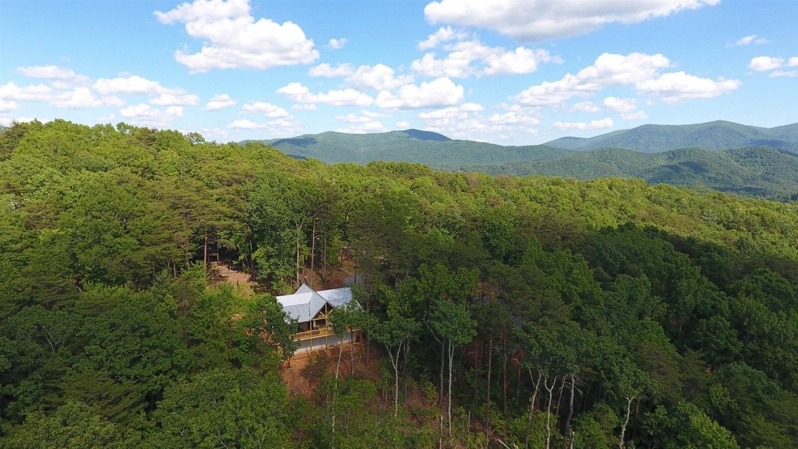 A cabin surrounded by dense forest with a clear view of distant mountains.