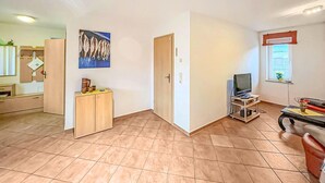 A spacious living room with a tiled floor, a wooden cabinet, a television on a stand, and a painting on the wall. - Ferienwohnung Kölpinsee/Usedom (Kölpinsee/Usedom)