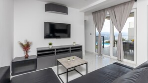 En moderne stue med et fladskærms-tv, en grå sofa, et sofabord og en balkon med udsigt.