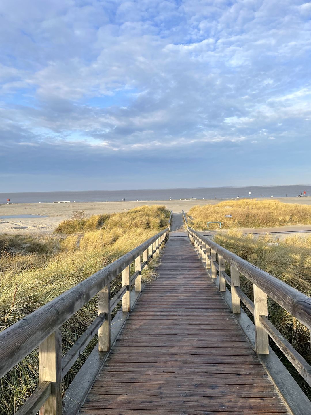 A wooden boardwalk leading to a beach with dunes and a cloudy sky.