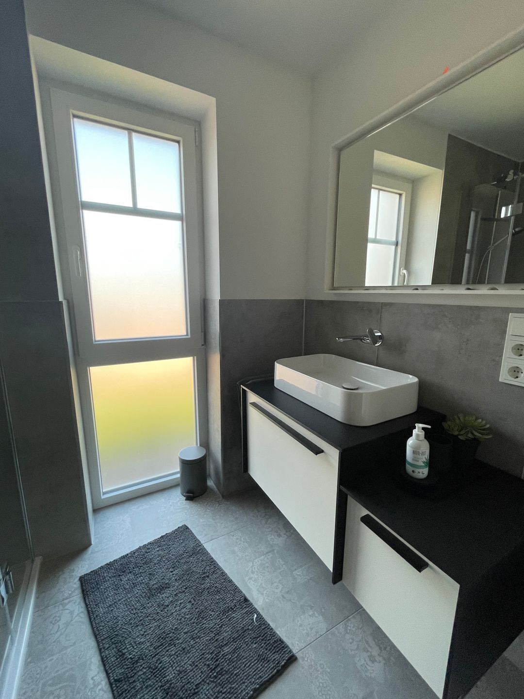 A modern bathroom with a large window, a sink, and a mirror.