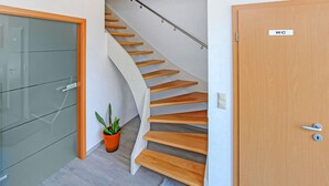 A modern interior with a wooden staircase, a glass cabinet, and a door labeled "WC". - Ferienwohnung Zwiedorf (Zwiedorf)