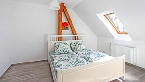A bedroom with a sloped ceiling, a bed with floral bedding, a white radiator, and a window with a view of trees. - Ferienwohnung Zwiedorf (Zwiedorf)