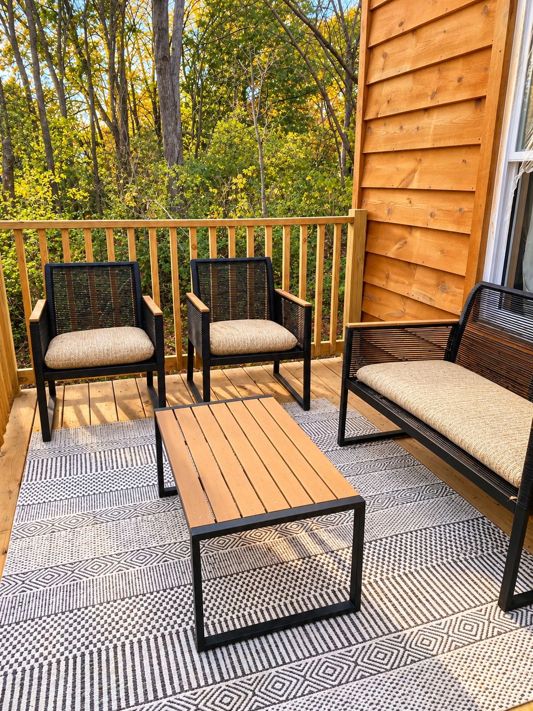 A wooden deck with two chairs and a bench, a patterned rug, and a wooden wall.