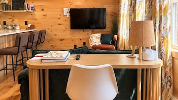 A cozy living area with a wooden floor, a sofa, a TV, and a table with chairs.