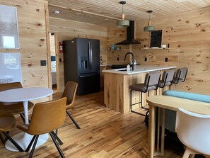 A compact kitchen with a black refrigerator, wooden cabinets, a sink, and a small dining area with chairs and a table. - 1 Bdr Cabin duplex unit on Apple River. Kayaks, SUPs & Sauna. Pet friendly! (Amery)