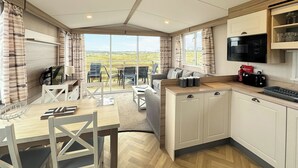 A modern kitchen with a dining area, large windows, and a view of the countryside. - 3 bedroom accommodation in Sandgreen (Sandgreen)