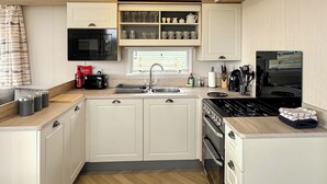 A compact kitchen with a microwave, toaster, sink, stove, and cabinets. - 3 bedroom accommodation in Sandgreen (Sandgreen)