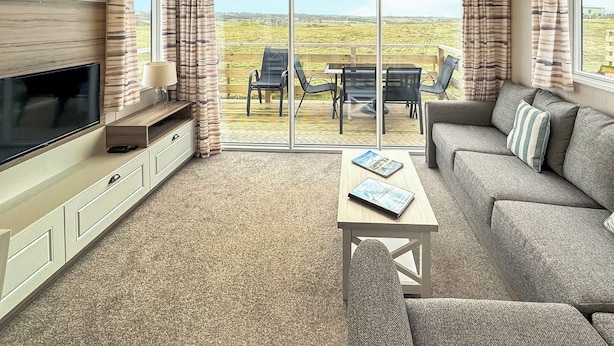 A living room with a TV, sofa, coffee table, and a view of the outdoors. - 3 bedroom accommodation in Sandgreen (Sandgreen)