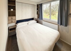 Une chambre à coucher comprenant un lit, des étagères intégrées, une fenêtre avec des rideaux et un radiateur.