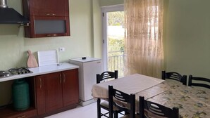Une cuisine compacte avec des meubles en bois, une cuisinière à gaz, un petit réfrigérateur et une table à manger avec des chaises.