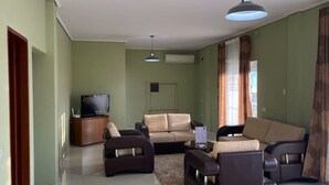 Un salon comprenant un canapé, deux fauteuils, une table basse, un téléviseur et un luminaire au plafond.