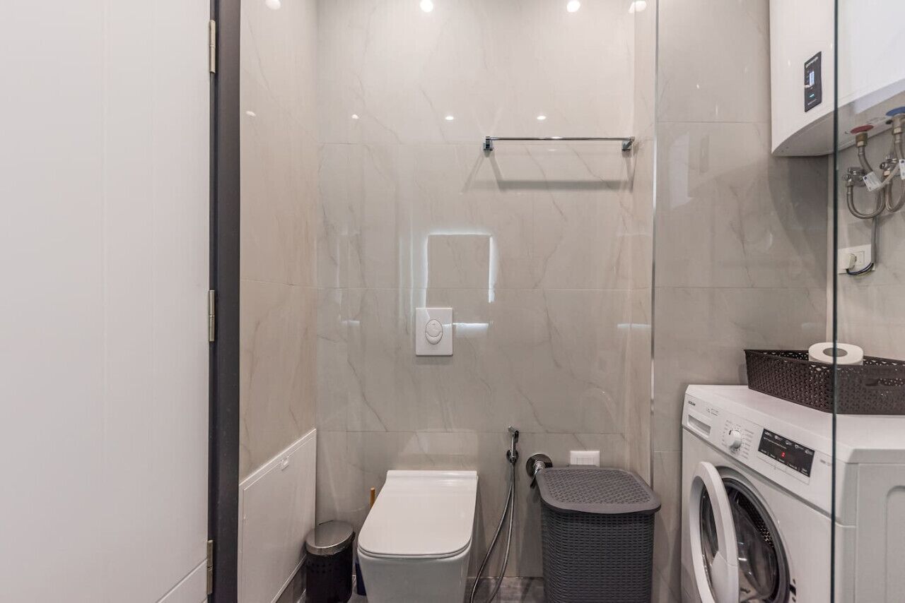 Une petite salle de bain comprenant des toilettes, un lave-linge et une petite poubelle.