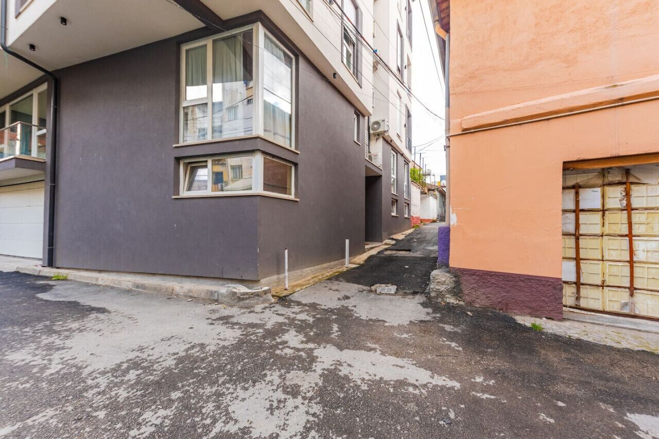 Una calle estrecha con un edificio a la izquierda y un coche aparcado a la derecha.