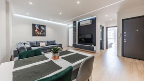 Una sala de estar moderna con un sofá, una mesa de comedor con sillas, un televisor de pantalla plana y una planta en maceta.