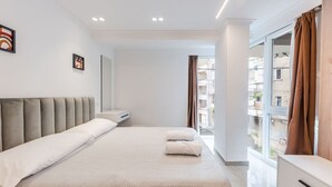 Una habitación de hotel moderna con una cama grande, una mesita de noche, una cómoda y una ventana con cortinas.