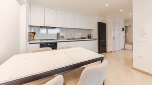 Una cocina moderna con armarios blancos, una mesa de comedor con sillas y un refrigerador negro.