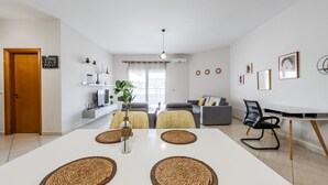 A modern living room with a white dining table, grey sofa, and a black office chair.