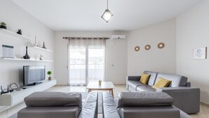 A modern living room with a grey sofa, a coffee table, and a TV on a white console.