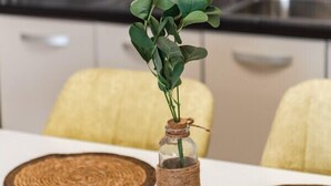 A dining table with a clear glass vase containing green leaves, surrounded by woven placemats.