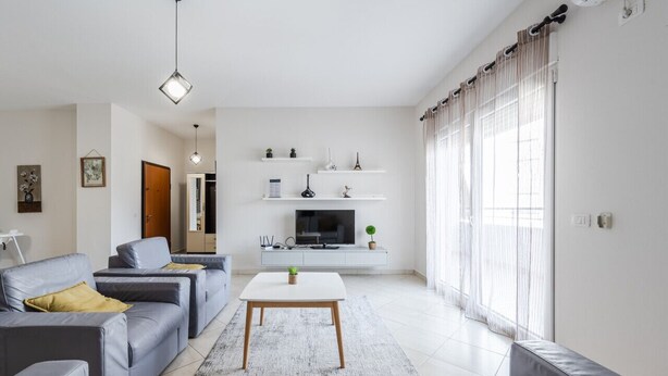 A modern living room with grey sofas, a white coffee table, and a TV on a white console.