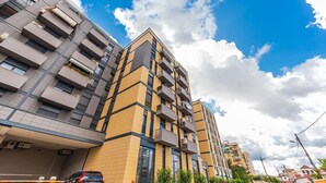 Un immeuble résidentiel à plusieurs étages, doté de balcons, d’un espace de stationnement et surplombant un ciel dégagé.