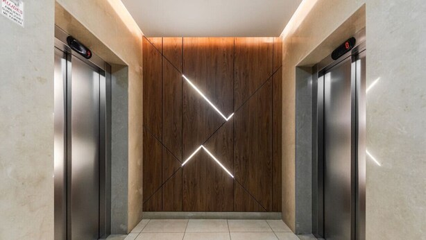 Un ascenseur dont les parois sont recouvertes de panneaux en bois et qui présente un éclairage au design géométrique.