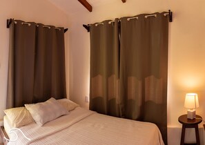 Une chambre d’hôtel avec un lit, des rideaux, une table de chevet et une lampe.