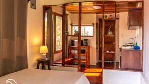 Ein Hotelzimmer mit Bett, Schreibtisch, Stuhl, Lampe, Ablage mit Handtüchern und Blick ins Freie.