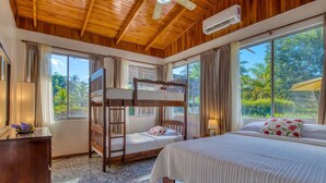 A room with a bunk bed, a single bed, a desk, and a window with a view of greenery. - Fully Equipped Bungalow 2 (Parrita)