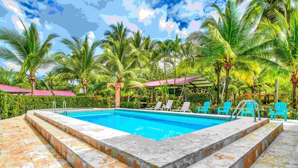 A swimming pool with steps leading up to it, surrounded by palm trees and blue chairs. - Fully Equipped Bungalow 2 (Parrita)