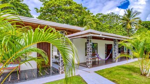 A modern house with a covered porch, stone pillars, and lush tropical landscaping. - Fully Equipped Bungalow 2 (Parrita)
