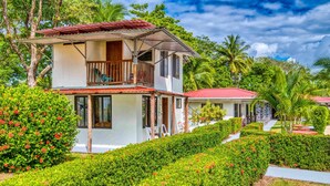 A two-story building with a balcony, surrounded by lush greenery and palm trees. - Fully Equipped Bungalow 2 (Parrita)