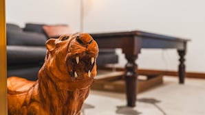 Een houten beeld van een tijger in een kamer met een donkergroene bank en een houten bijzettafeltje.