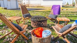 Een buitenzitgedeelte met houten stoelen en een vuurkuil.
