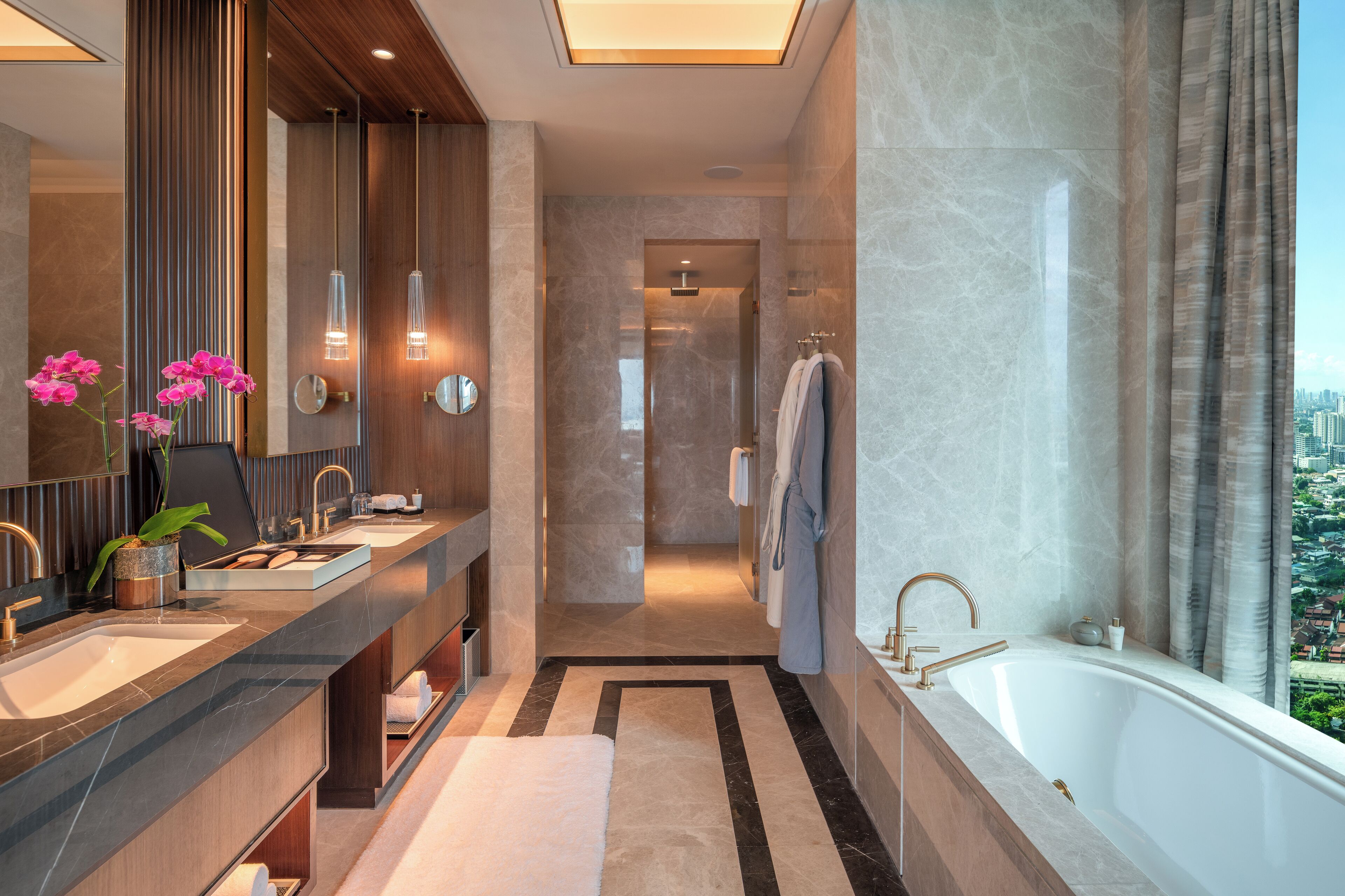 A modern bathroom with dual sinks, a large bathtub, and a city view.