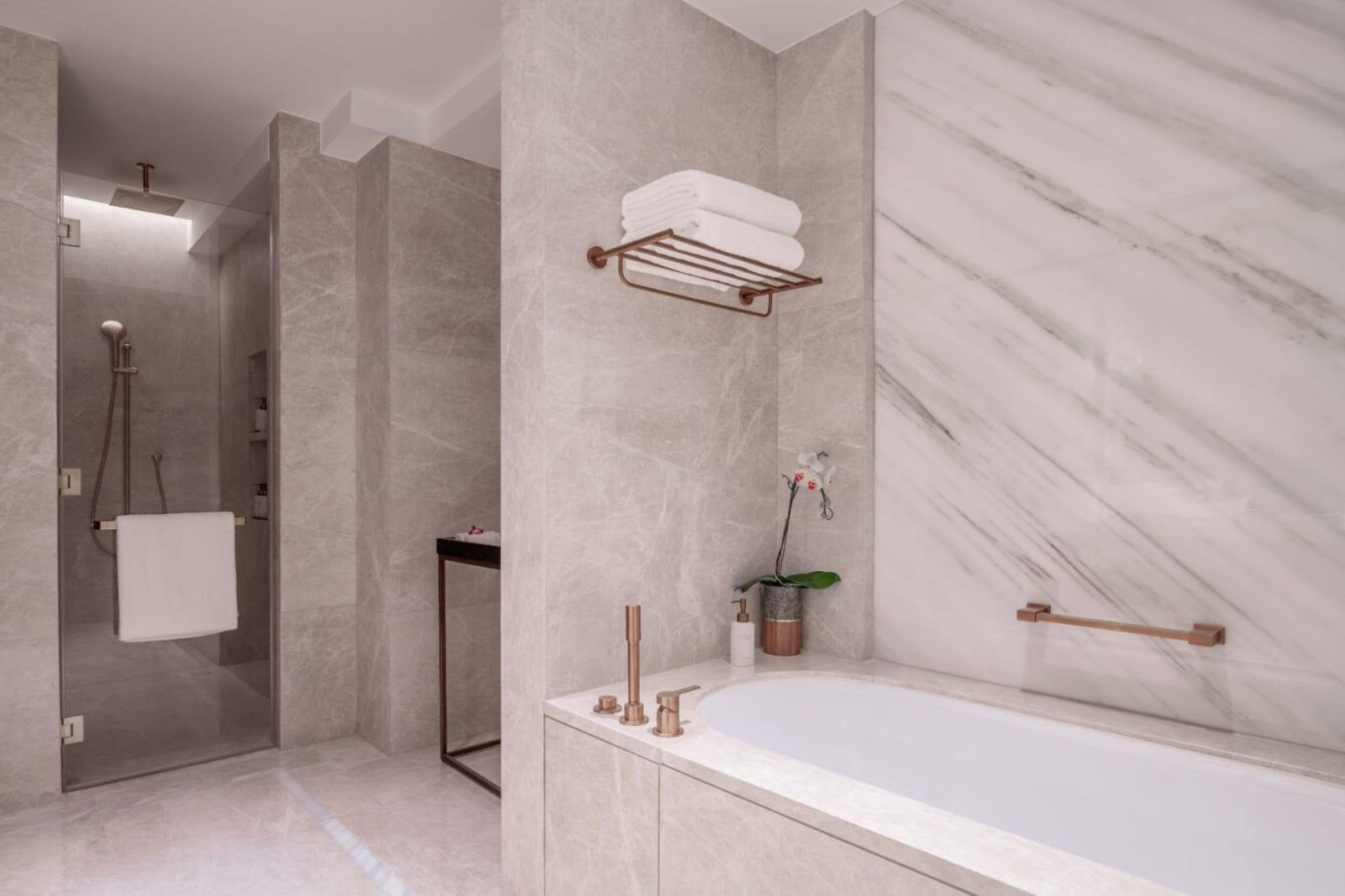 A modern bathroom with a marble wall, a bathtub, a towel rack, and a shower area.