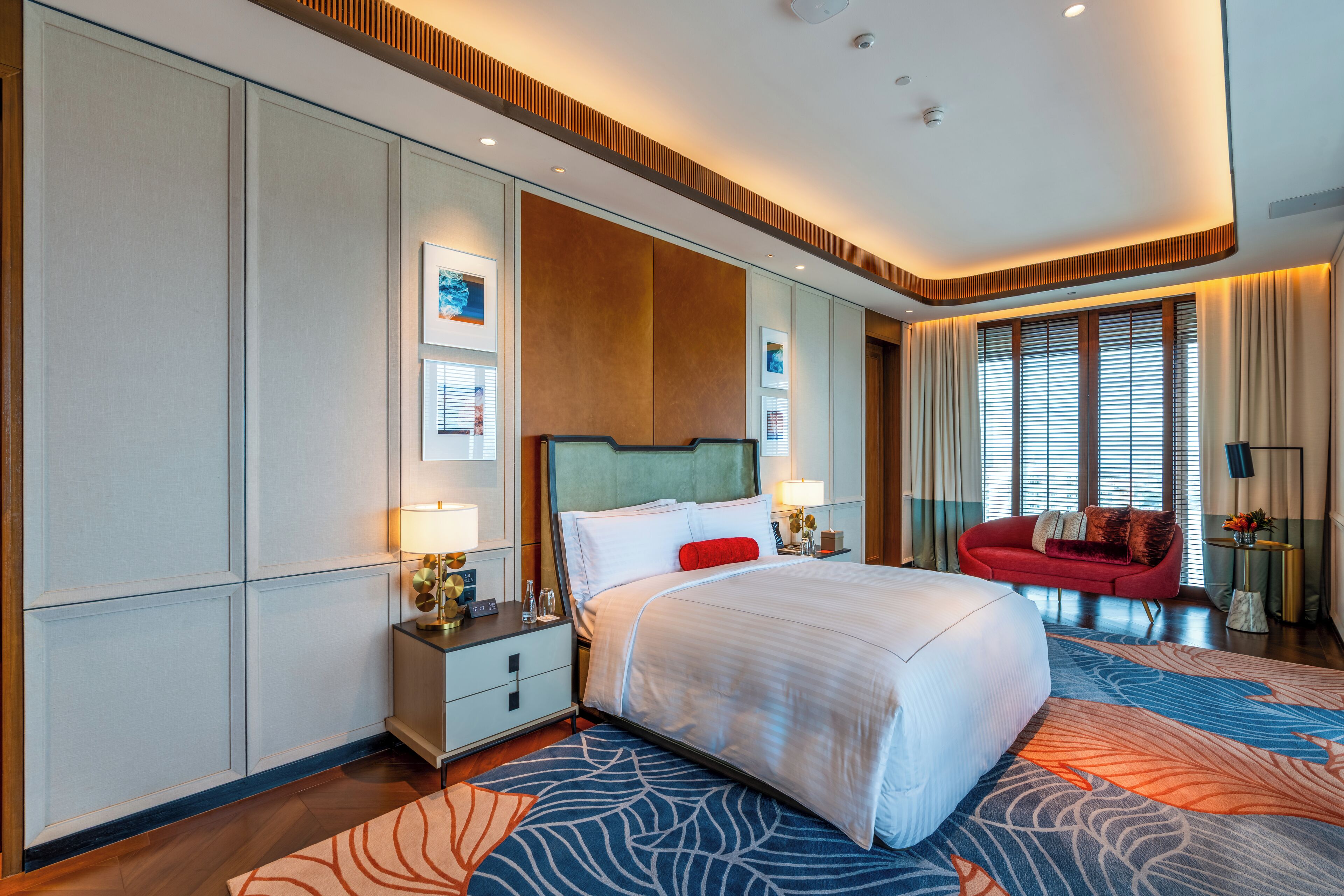 Habitación de hotel moderna con una cama grande, un sofá rojo y vistas de la ciudad a través de amplias ventanas.