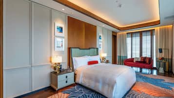 A modern hotel room with a large bed, a red sofa, and a view of the city through large windows.