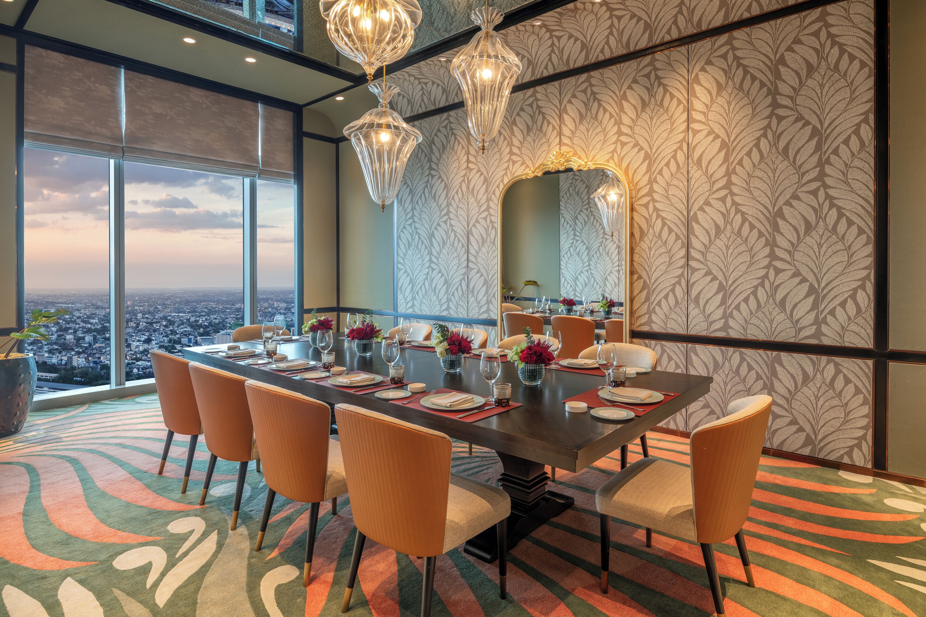 Un comedor con vista a la ciudad, ventanas amplias y un papel tapiz estampado.
