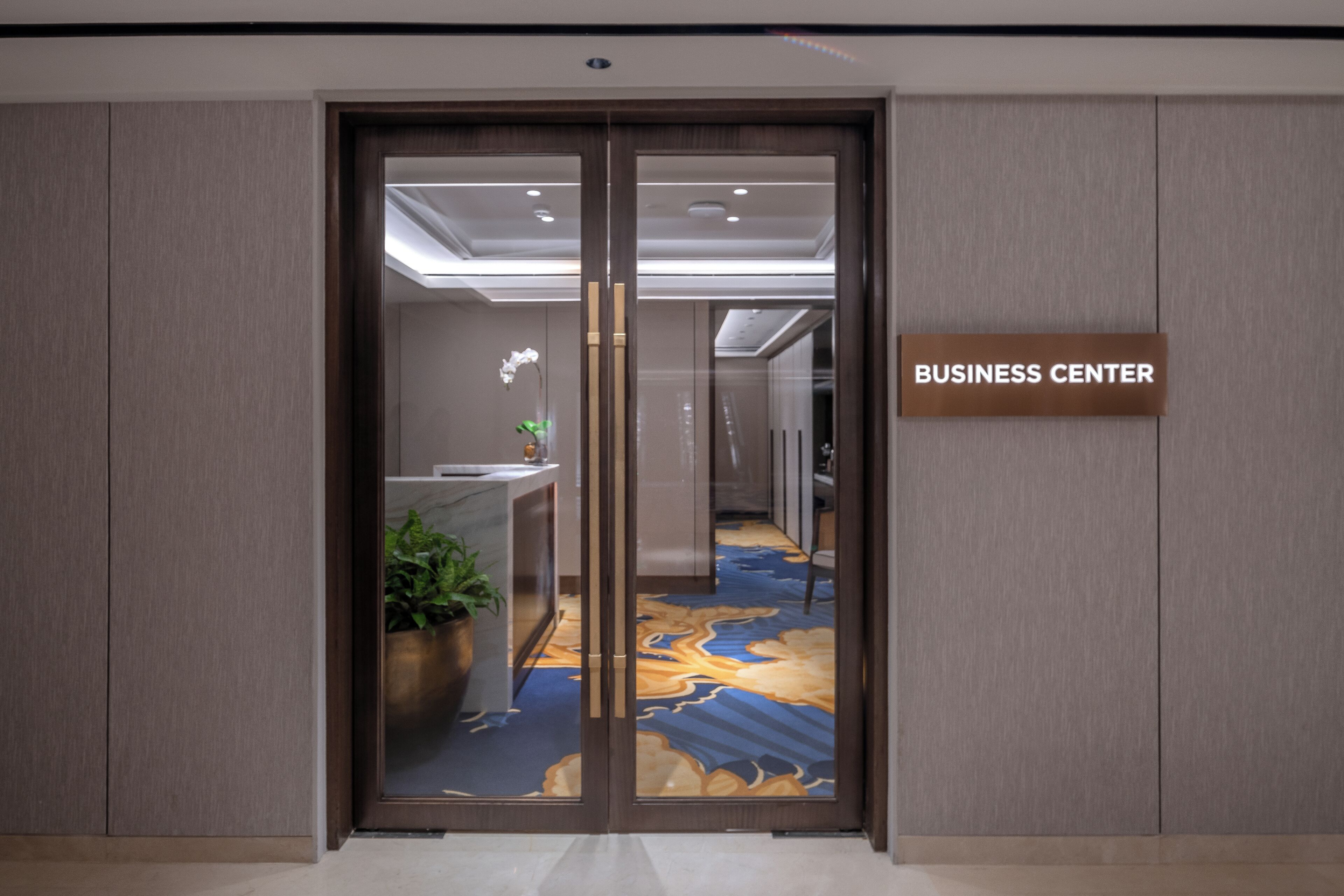 A modern business center entrance with a glass door, a reception desk, and a sign indicating the location.