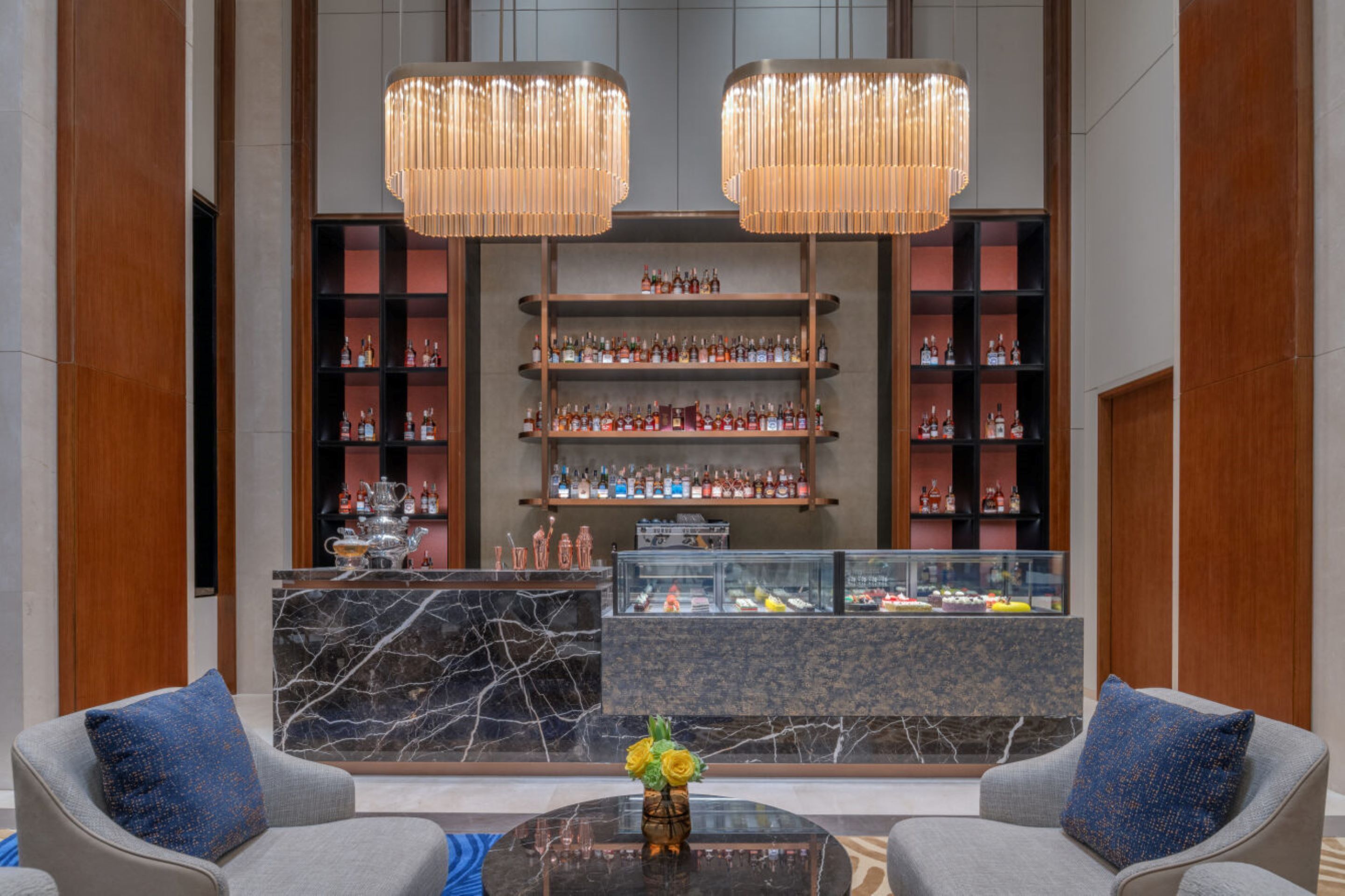 A lobby with two sofas, a marble reception desk, and shelves of liquor bottles.