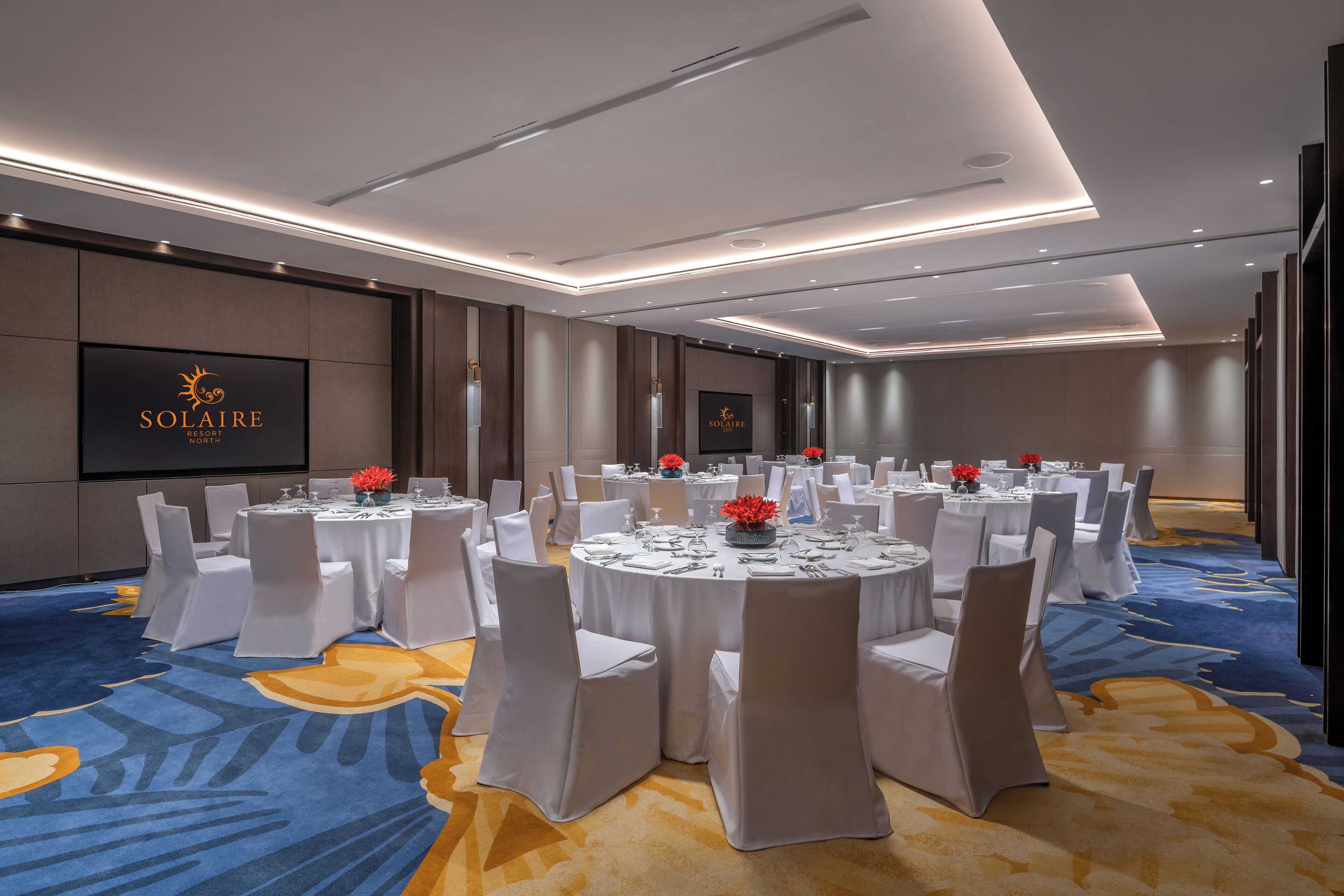 A conference room with round tables, white chairs, and a blue carpet.